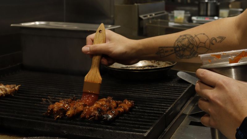 A person grilling barbecue skewers